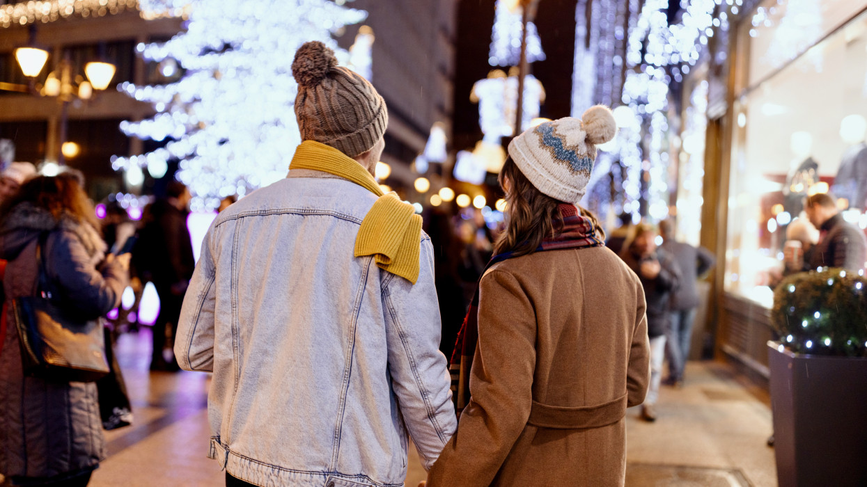 Happy couple holding hands and walking down city streets which are decorated with Christmas lights