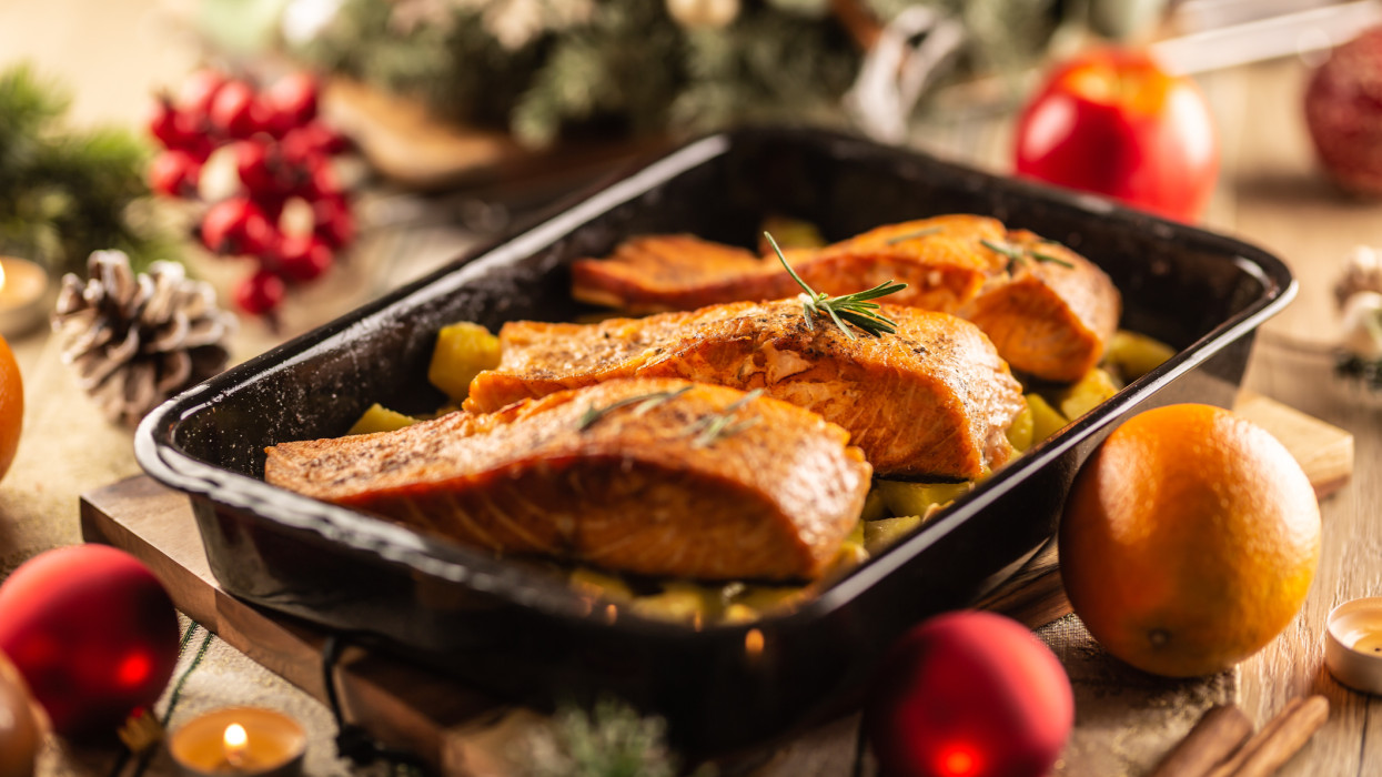 Baked festive meal of salmon in a baking tray surrounded by Christmas decoration.